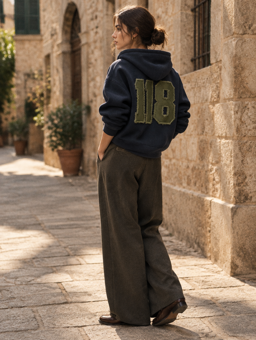 De 118 Zipped Hoodie gedragen in een zonovergoten steegje, met de Olive Branch patch zichtbaar op de rug